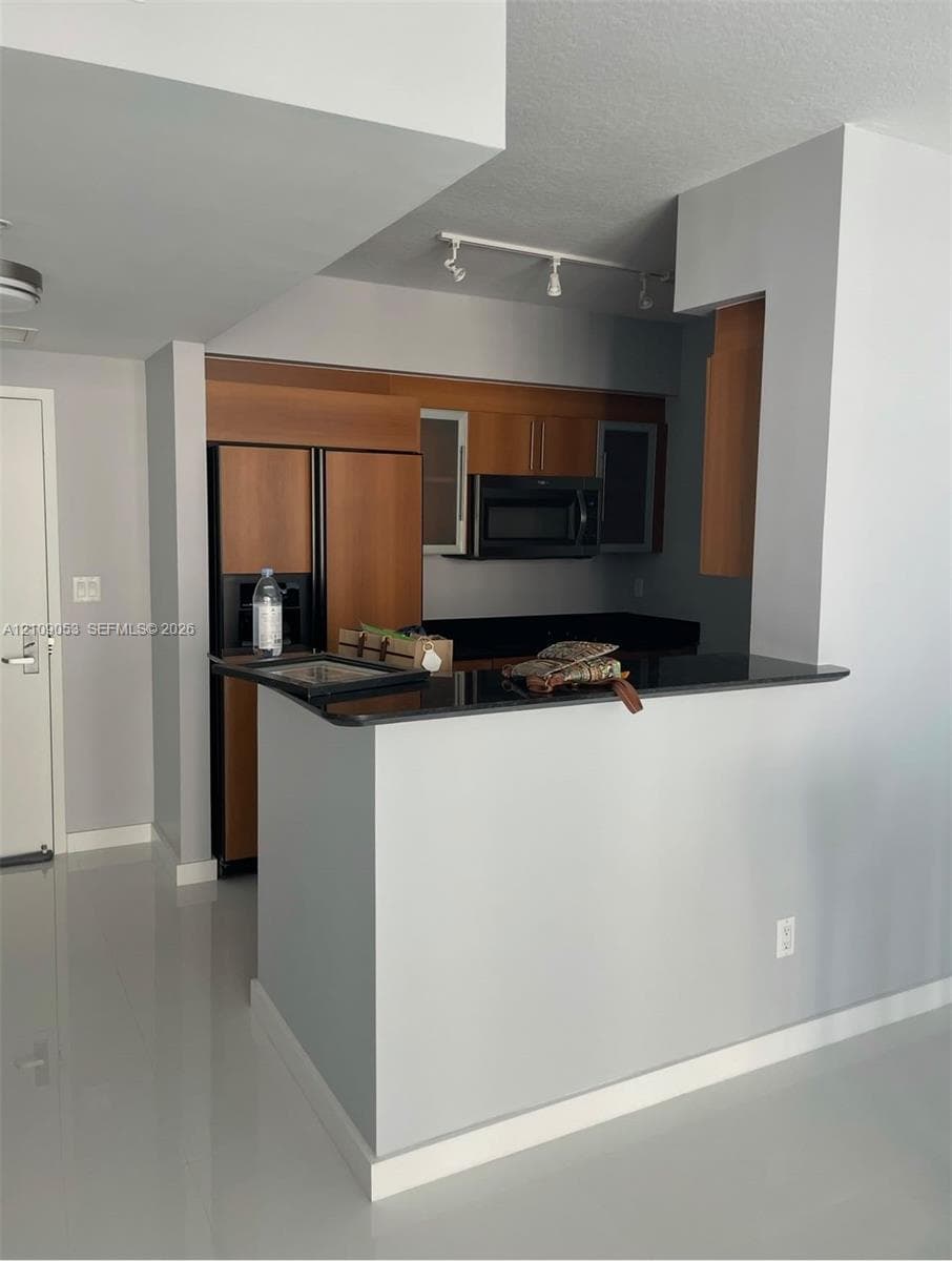 Kitchen featuring wood cabinetry, solid surface countertops, integrated appliances, track lighting, and glossy flooring