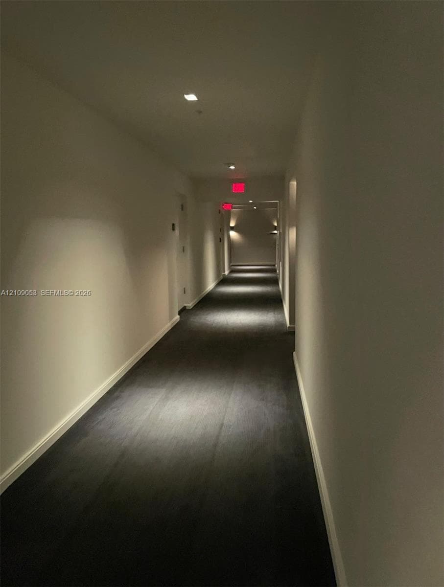 Neutral-toned hallway featuring recessed ceiling lighting, wall-mounted sconces, and dark carpeting