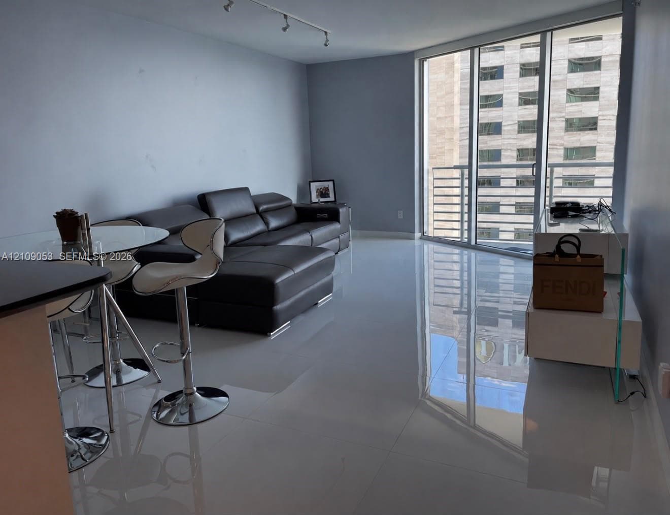Open-concept room featuring high-gloss flooring, track lighting, and floor-to-ceiling windows with balcony access
