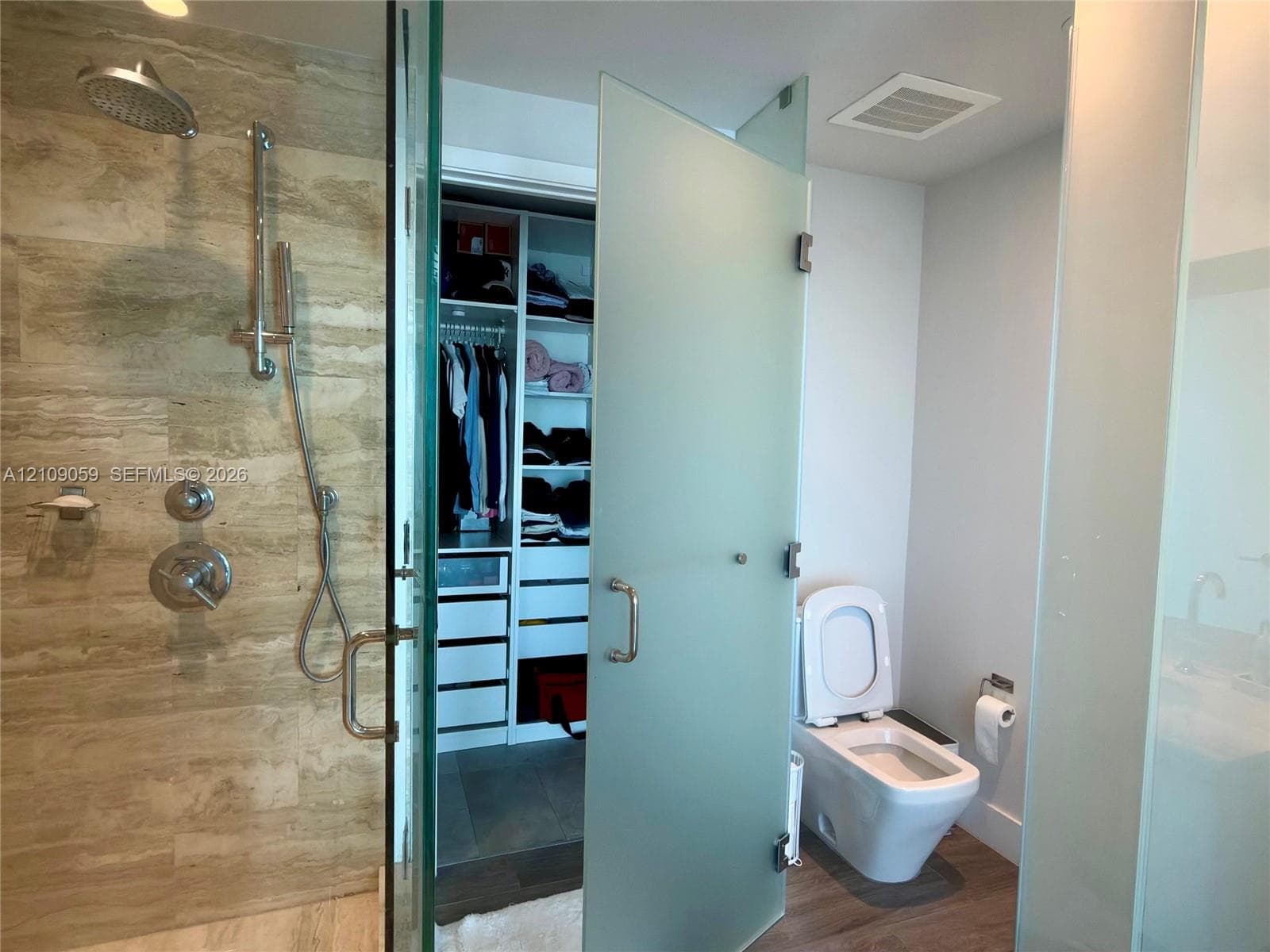 Walk-in shower with stone-tile surround, chrome wall-mounted fixtures, and glass door