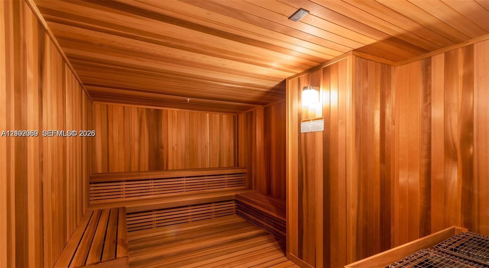 Sauna room featuring full wood-paneled walls and ceiling, built-in tiered wooden benches, and wall-mounted light fixture