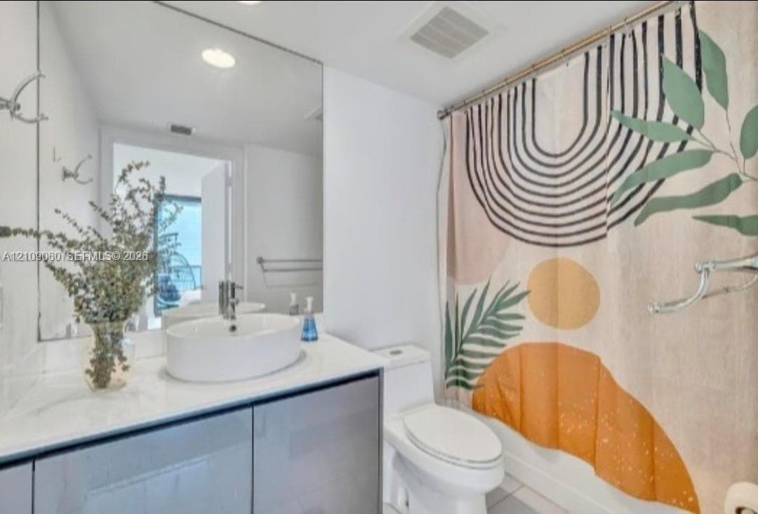 Bathroom featuring a vanity with a white countertop and oval vessel sink, complemented by a large wall-mounted mirror and polished chrome hardware