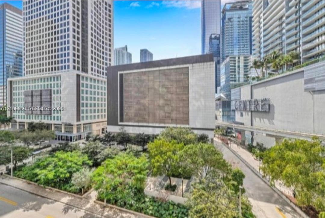 Urban setting featuring a multi-story facade with stone cladding and metallic accents, surrounded by mature greenery and landscaped vegetation