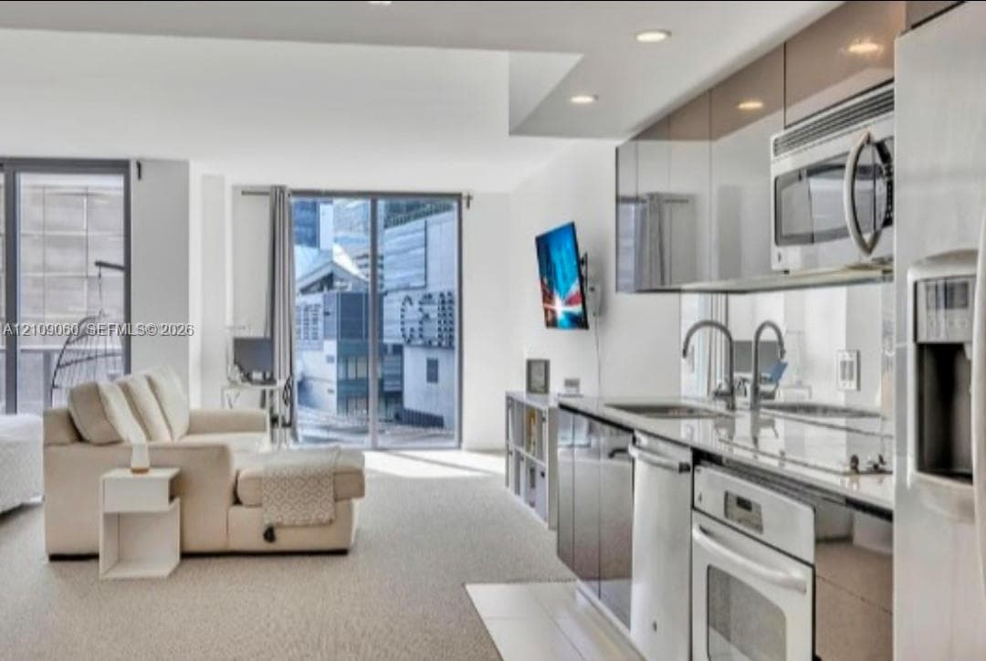 Kitchen featuring high-gloss cabinetry, stainless steel appliances, and quartz countertops, complemented by wall-to-wall glass windows and recessed lighting