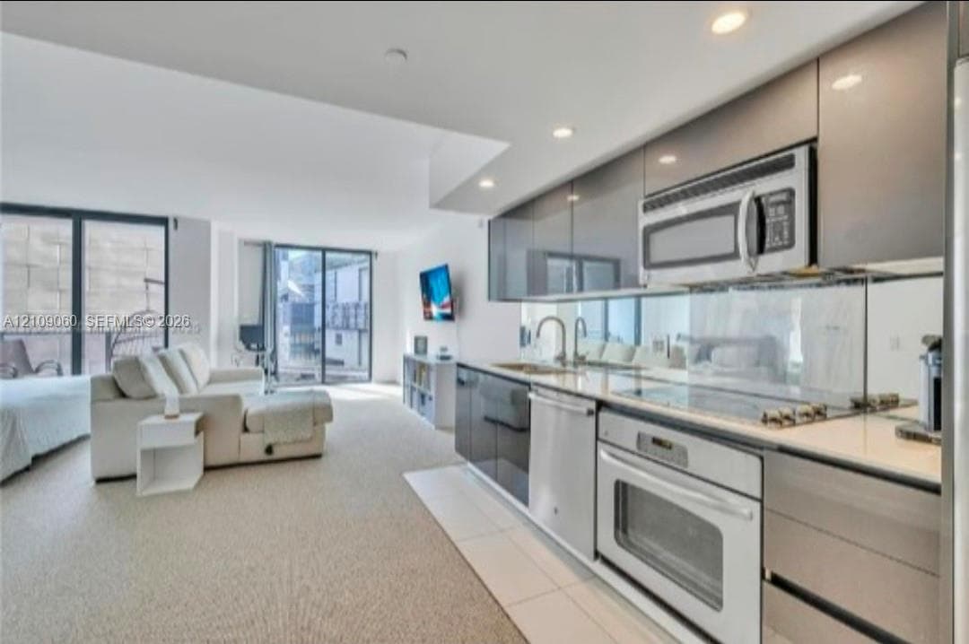 Kitchen featuring gloss-finish cabinetry, stainless steel appliances, mirror backsplash, and solid-surface countertops, accented by recessed lighting