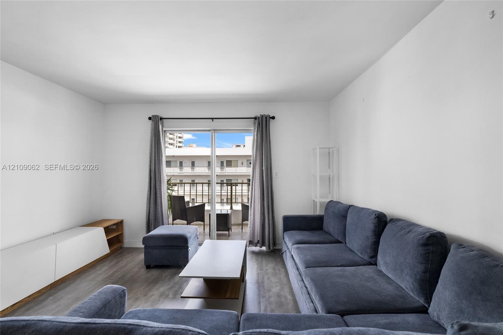Living area featuring wood-finish flooring, white walls, and a sliding glass door providing external access to a balcony with a metal railing