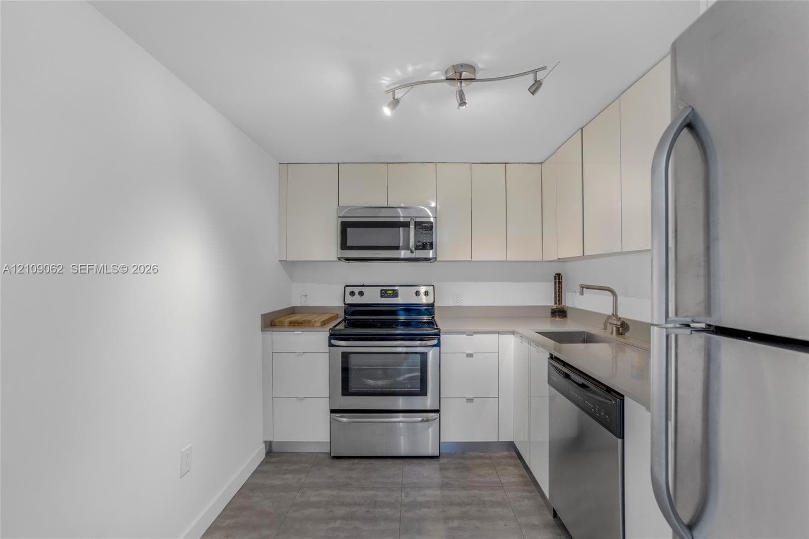 Kitchen featuring high-gloss flat-panel cabinetry, stainless steel appliances, solid-surface countertops, tile flooring, and adjustable multi-bulb track lighting