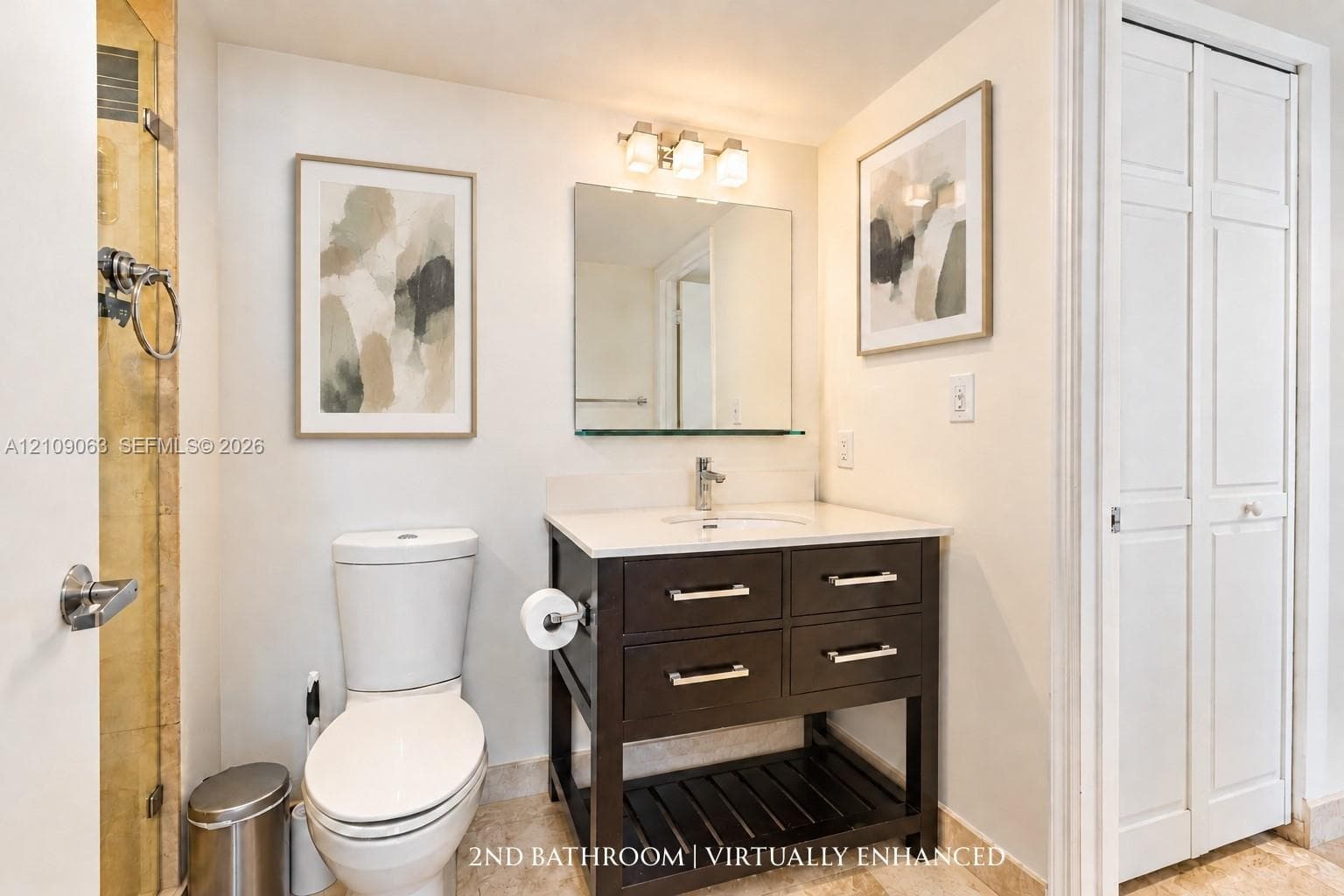 Vanity with a stone countertop and integrated sink, dark-finish cabinetry with silver-tone hardware, glass-enclosed shower, wall-mounted mirror, and tile flooring