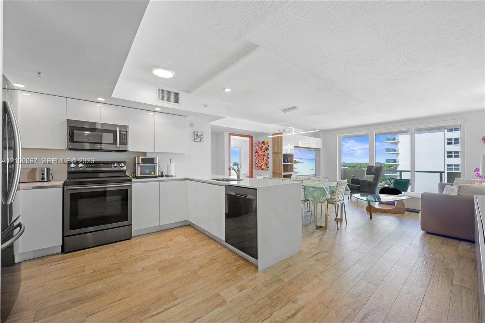 Modern kitchen featuring white flat-panel cabinetry, wood-finish flooring, quartz countertops, stainless steel appliances, and glass sliding doors