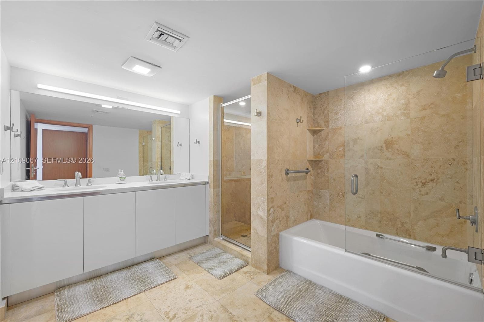 Double vanity with rectangular sinks, expansive wall-to-wall mirror, tiled soaking tub with glass partition, and separate walk-in shower featuring natural stone wall tile