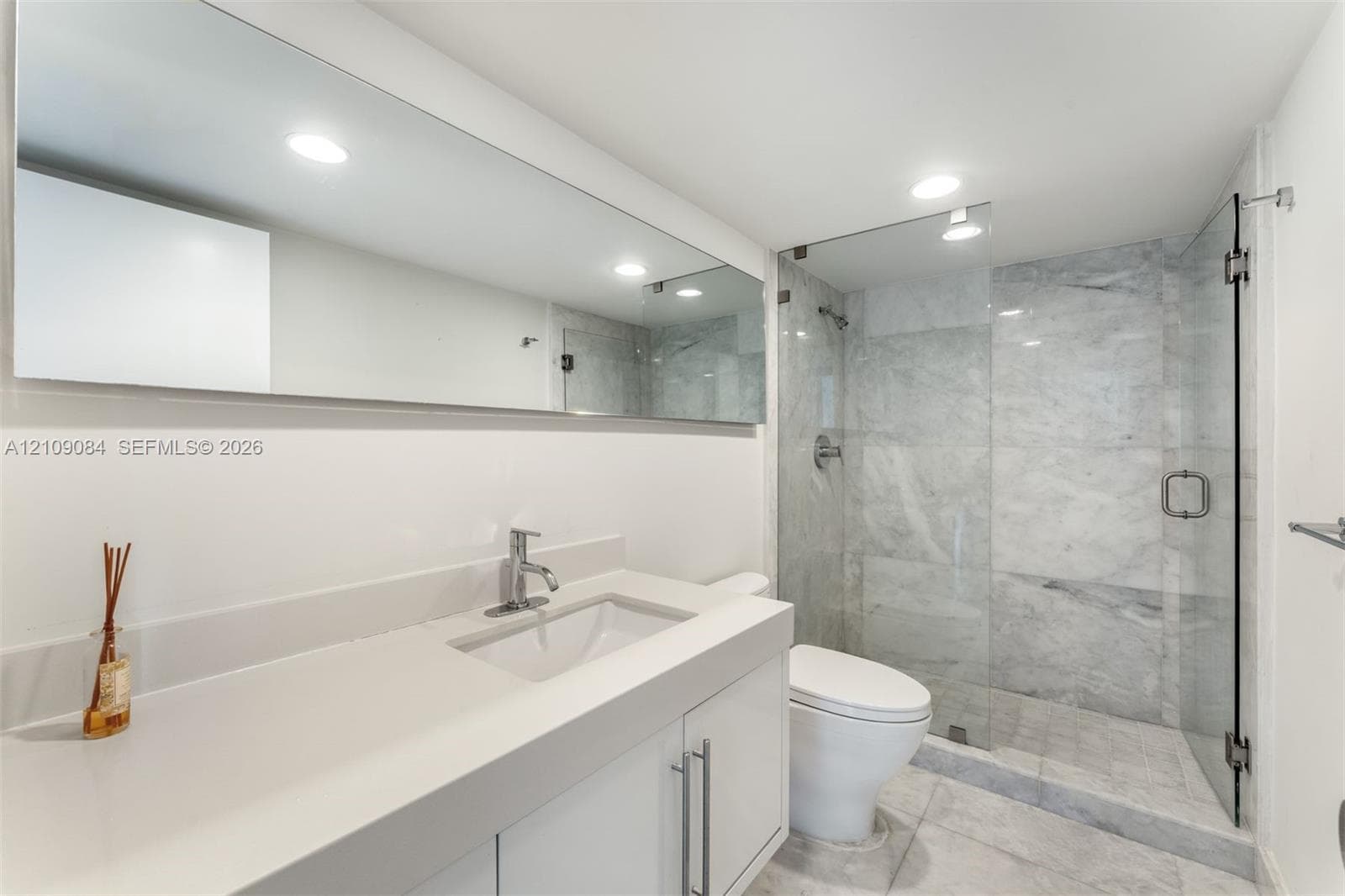 Exposed concrete ceilings, large-format tile flooring, wall-mounted track lighting, and full-height glass doors showcasing ocean scenery