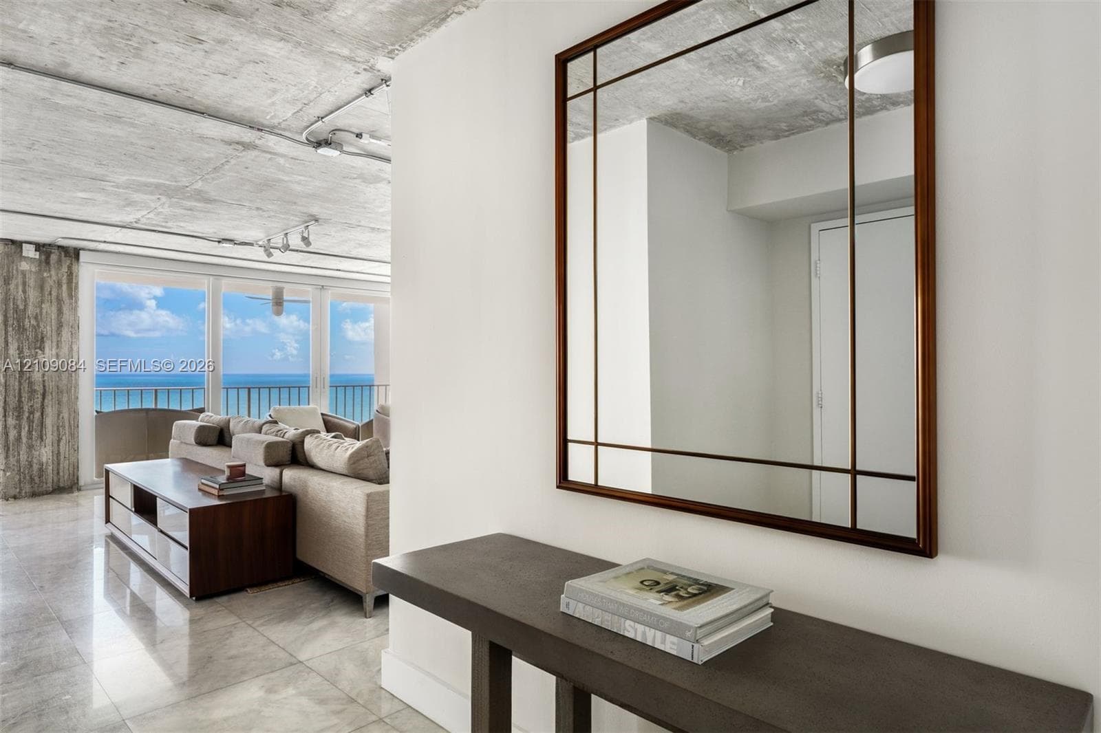 Exposed concrete ceiling, floor-to-ceiling glass paneling, stone-finish flooring, white flat-panel cabinetry, and a center island with a built-in wine refrigerator