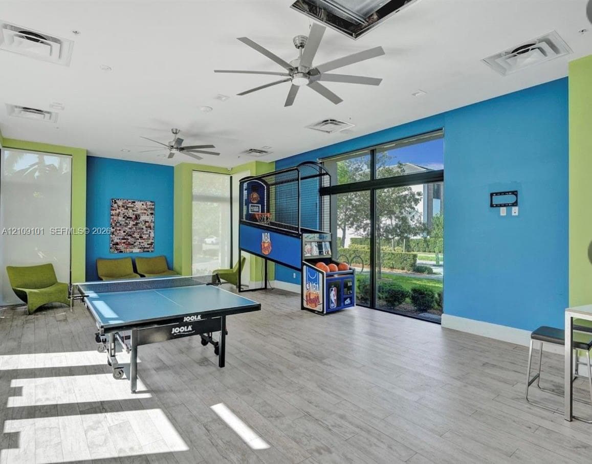Open-concept space featuring wood-finish flooring, floor-to-ceiling windows, and dual ceiling fans