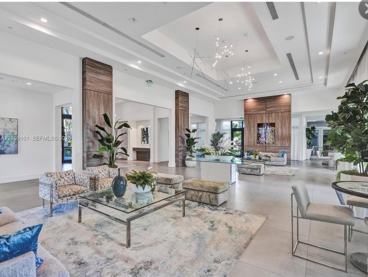 Large-scale interior featuring tiered tray ceilings, wood-paneled accent columns, recessed lighting, and contemporary branching chandeliers