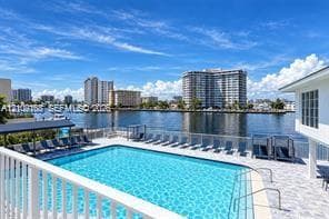 Waterfront swimming pool with tiled pool deck, metal safety railing, and surrounding perimeter fencing