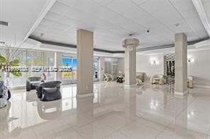 Expansive lobby featuring polished tile flooring, tray ceilings with recessed lighting, structural support columns, wall-mounted accent lighting, and floor-to-ceiling glass paneling
