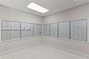 Secure metal mail center featuring a high-density, multi-compartment wall-mounted unit with recessed drop-ceiling lighting and neutral tile flooring