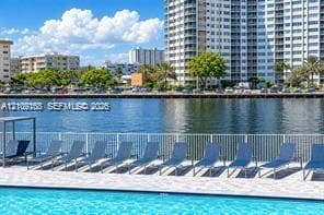 Waterfront swimming pool area featuring a paved deck, perimeter metal fencing, and water-level bulkhead