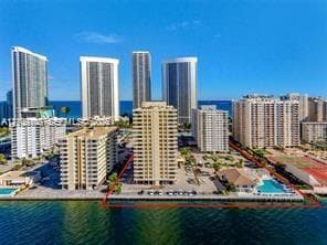 Waterfront high-rise property featuring an outdoor swimming pool, paved parking areas, and manicured landscaping