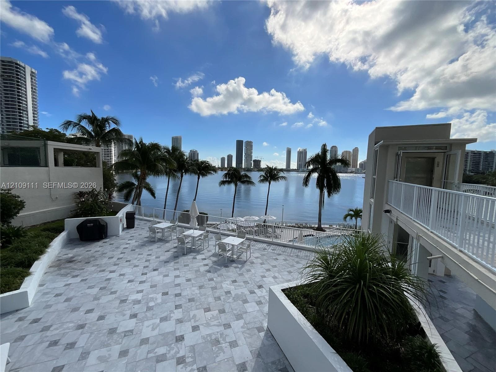 Expansive stone-paved terrace featuring white masonry planter boxes, perimeter metal railings, and elevated walkway access