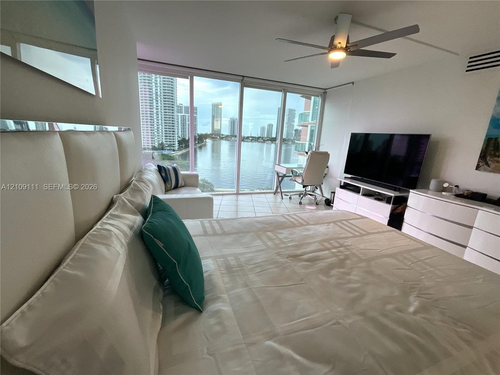 Floor-to-ceiling windows featuring urban water and skyline scenery, tile flooring, and a ceiling fan