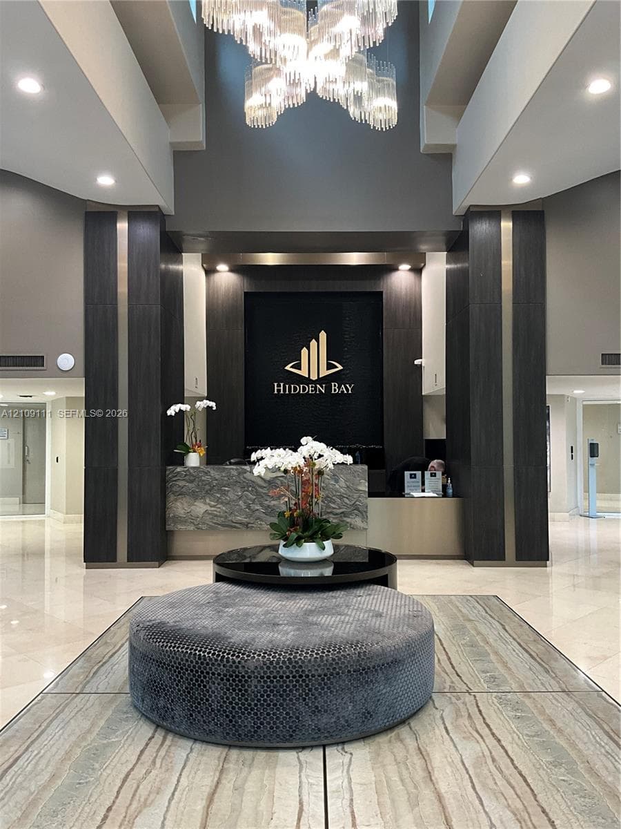 Grand lobby featuring a tiered crystal chandelier, stone-finish reception desk, recessed lighting, and polished stone flooring with vertical wood-paneled accents