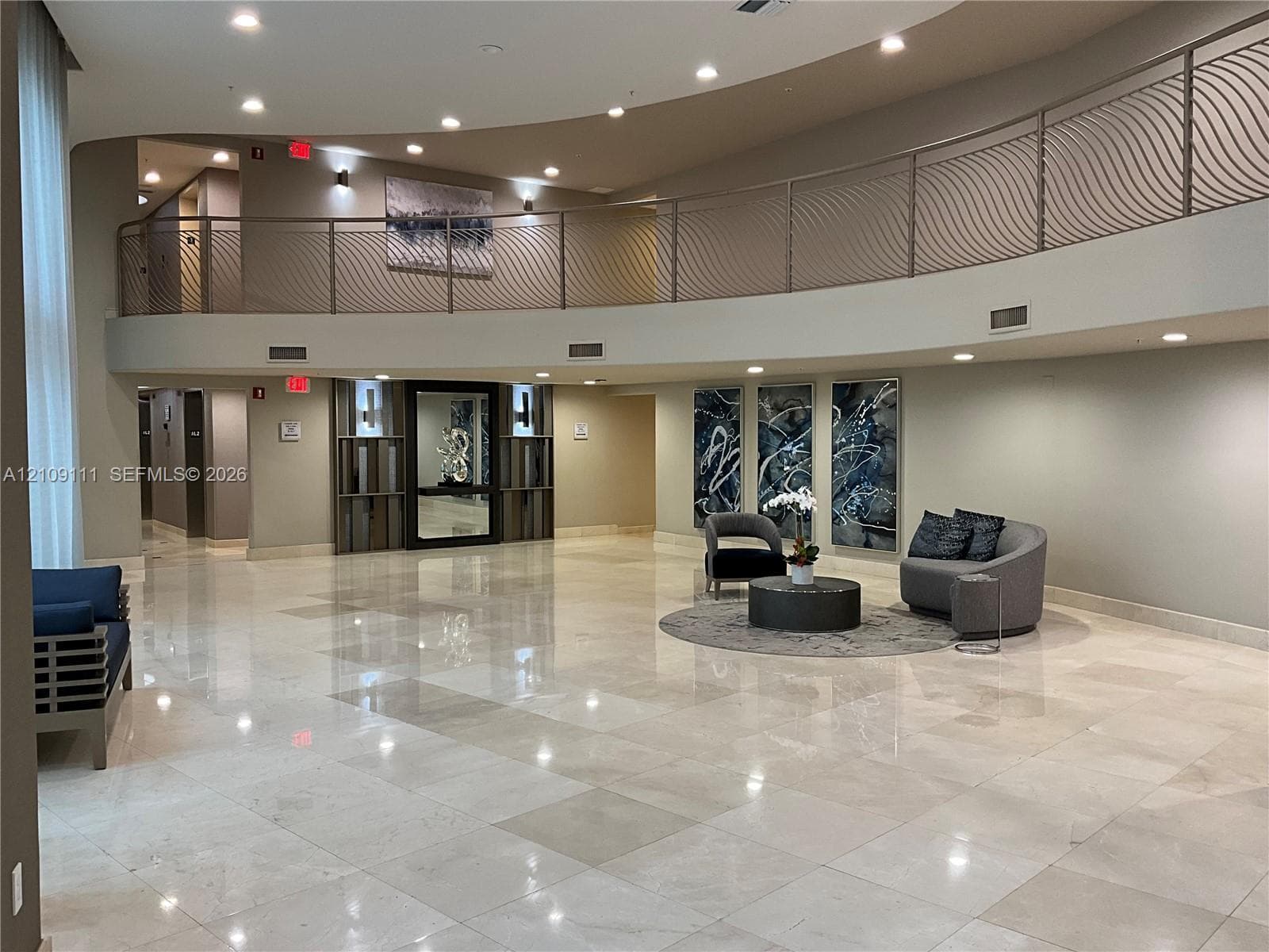 Double-height foyer featuring polished stone flooring, a curved mezzanine with decorative metal railing, recessed ceiling lighting, and built-in wall paneling