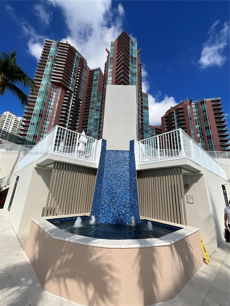 Cascading water feature with blue mosaic tiling, multi-story high-rise architecture, white metal railings, and concrete hardscaping