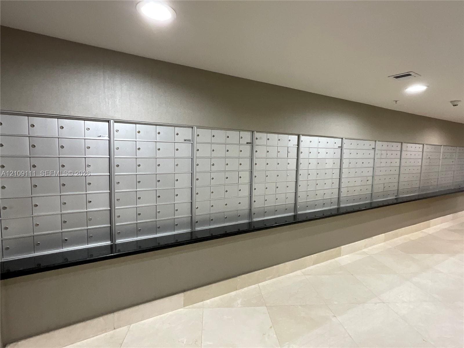 Wall-mounted metallic mailbox bank with a black solid surface counter and light-toned tile flooring