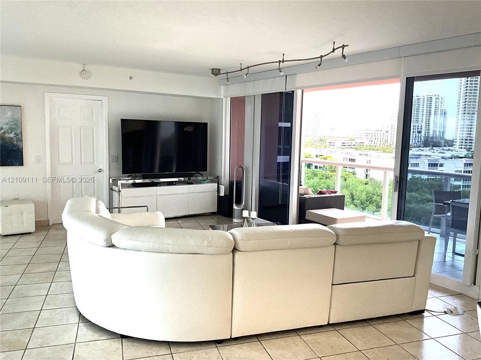 Large tile flooring, track lighting, and floor-to-ceiling sliding glass doors opening to a private balcony