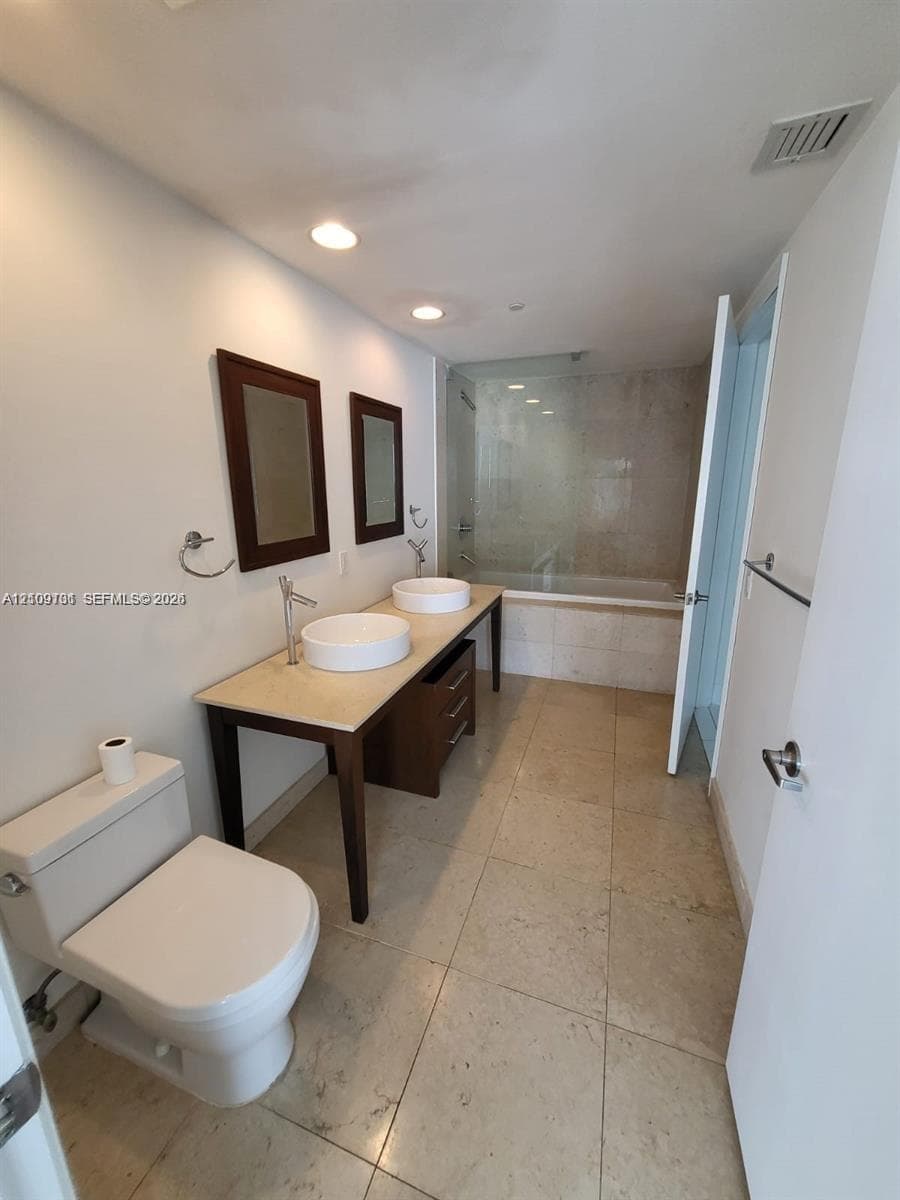 Dual-vanity bathroom featuring a stone-topped console, two elevated circular sinks, polished chrome fixtures, and a shower-tub combination with a glass enclosure