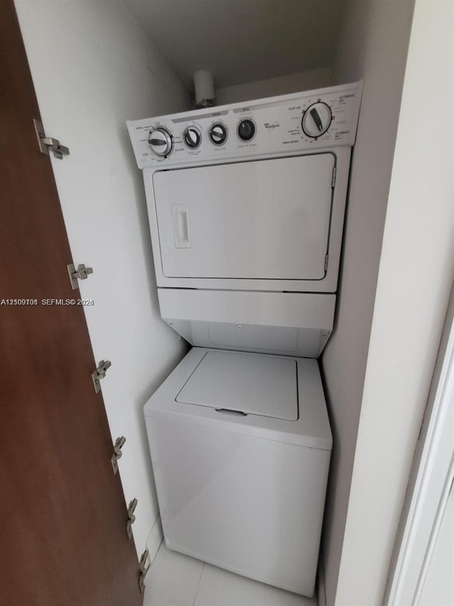 Stacked laundry unit featuring a white top-load washer and integrated dryer