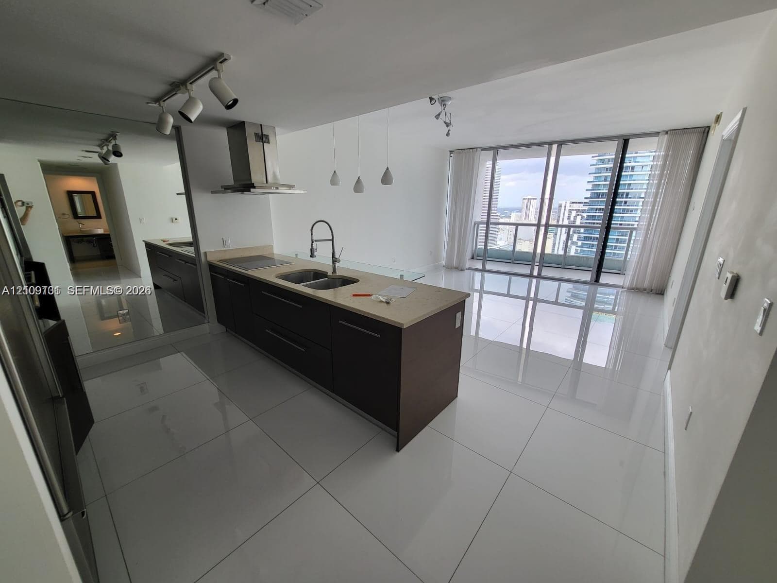 Kitchen featuring dark-toned cabinetry, a stone-surfaced island, stainless steel range hood, and porcelain tile flooring, complemented by floor-to-ceiling glass sliding doors