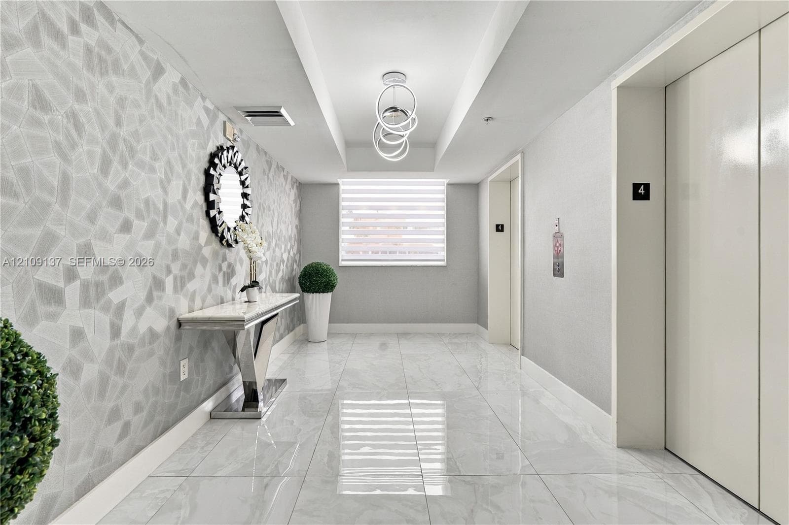 Entryway featuring large-format polished tile flooring, geometric textured wall covering, recessed ceiling detail, and contemporary ring chandelier