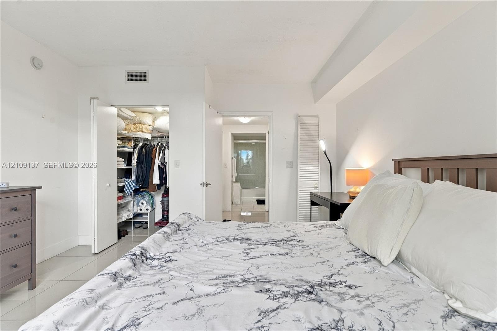 Neutral-toned room with tile flooring, featuring a walk-in closet with built-in shelving, louvered closet doors, and smooth ceiling finish