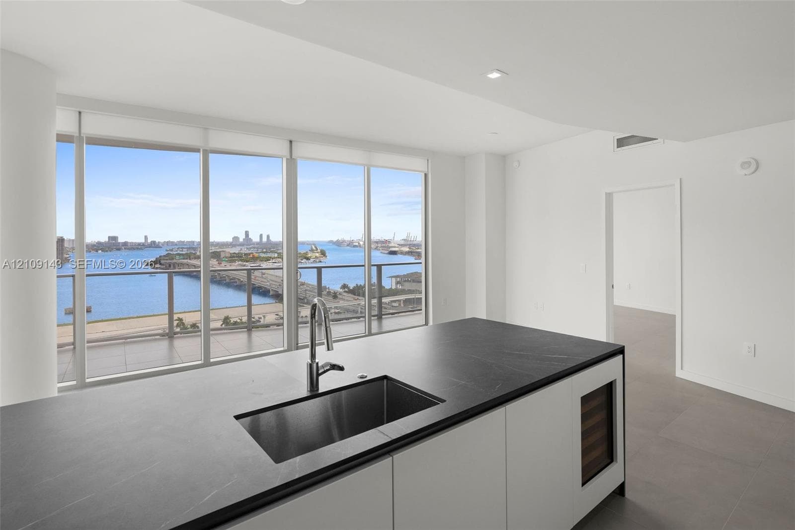Kitchen island featuring a dark stone countertop, undermount stainless steel sink, pull-down chrome faucet, built-in wine refrigeration, and floor-to-ceiling windows with water and skyline scenery