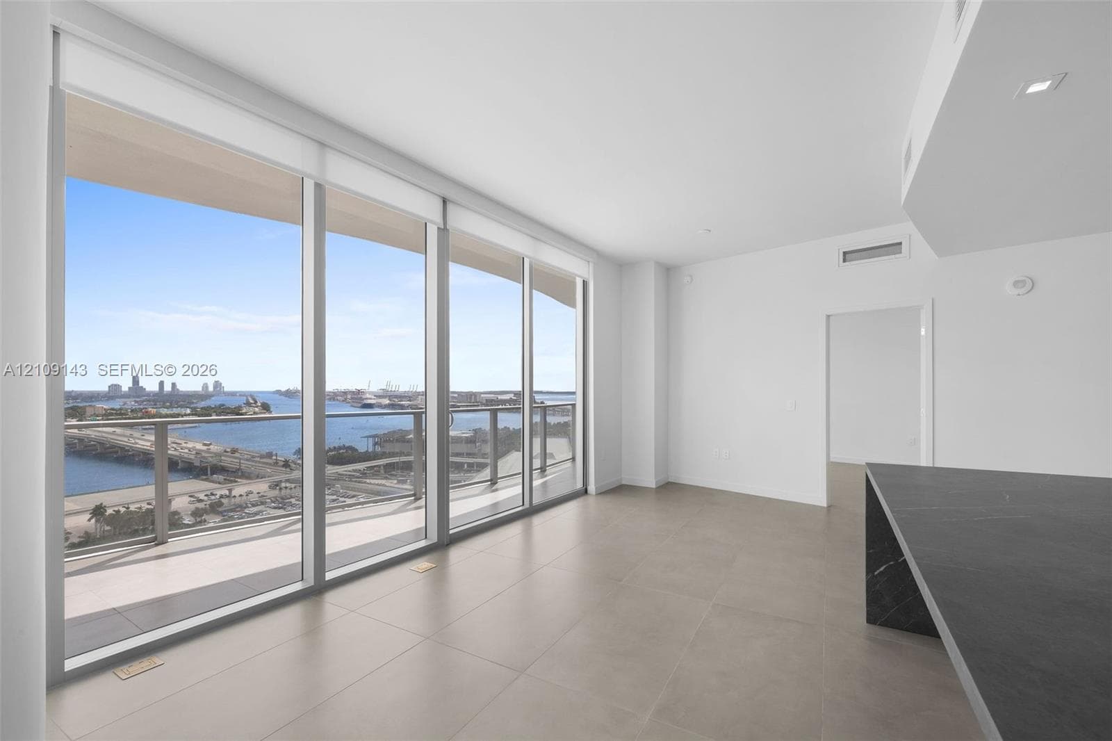 Floor-to-ceiling windows, private balcony with glass railing, large-format tile flooring, and built-in stone-top island