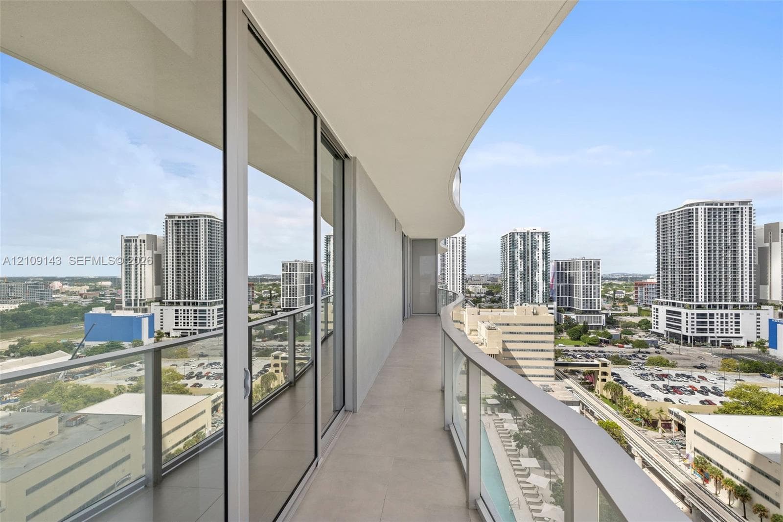 Curved balcony featuring tile flooring, glass panel railings, and floor-to-ceiling sliding glass doors