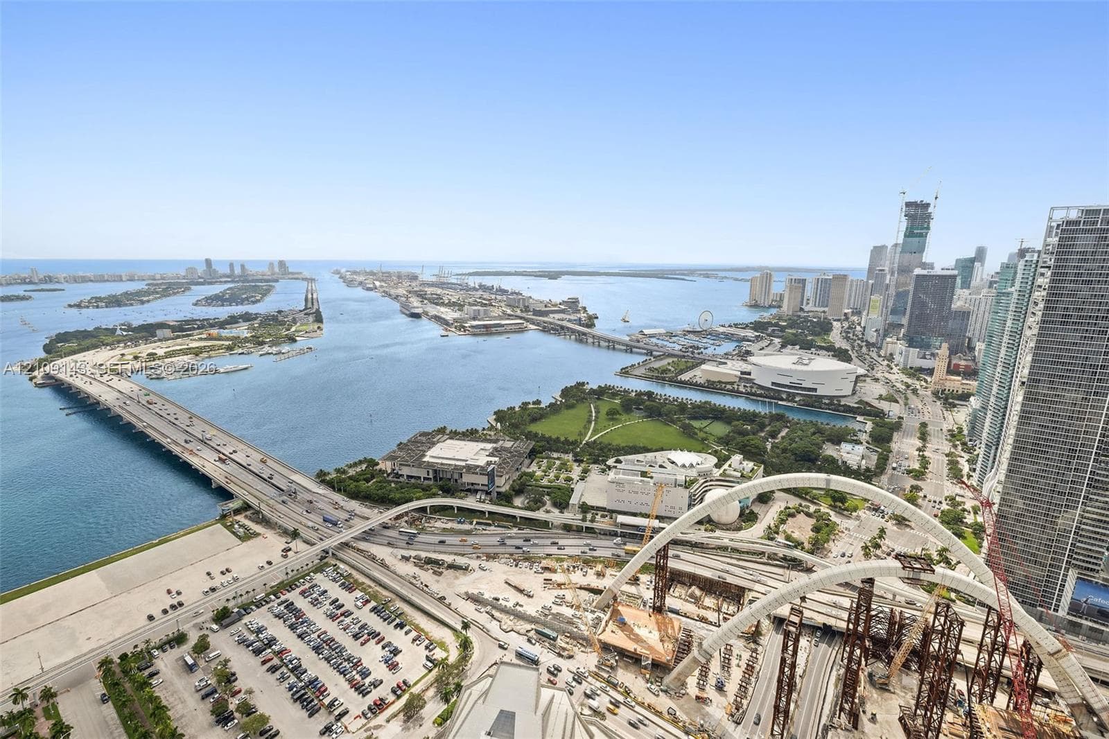 High-rise aerial perspective capturing coastal waterway, city skyline, expansive bridge infrastructure, and urban park space