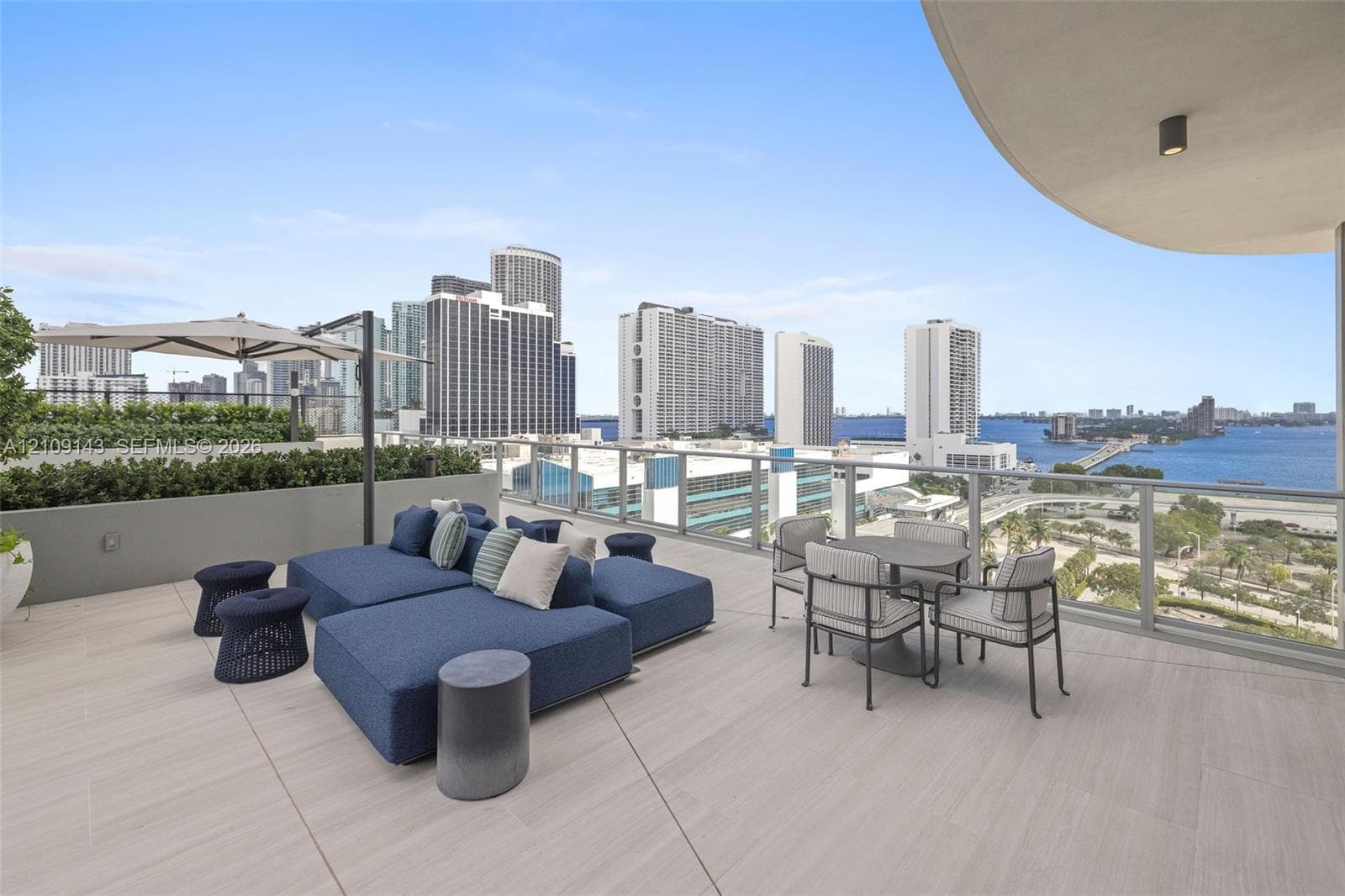Expansive open-air terrace featuring large-format tile flooring, perimeter privacy planters, and glass balcony railings with metal accents