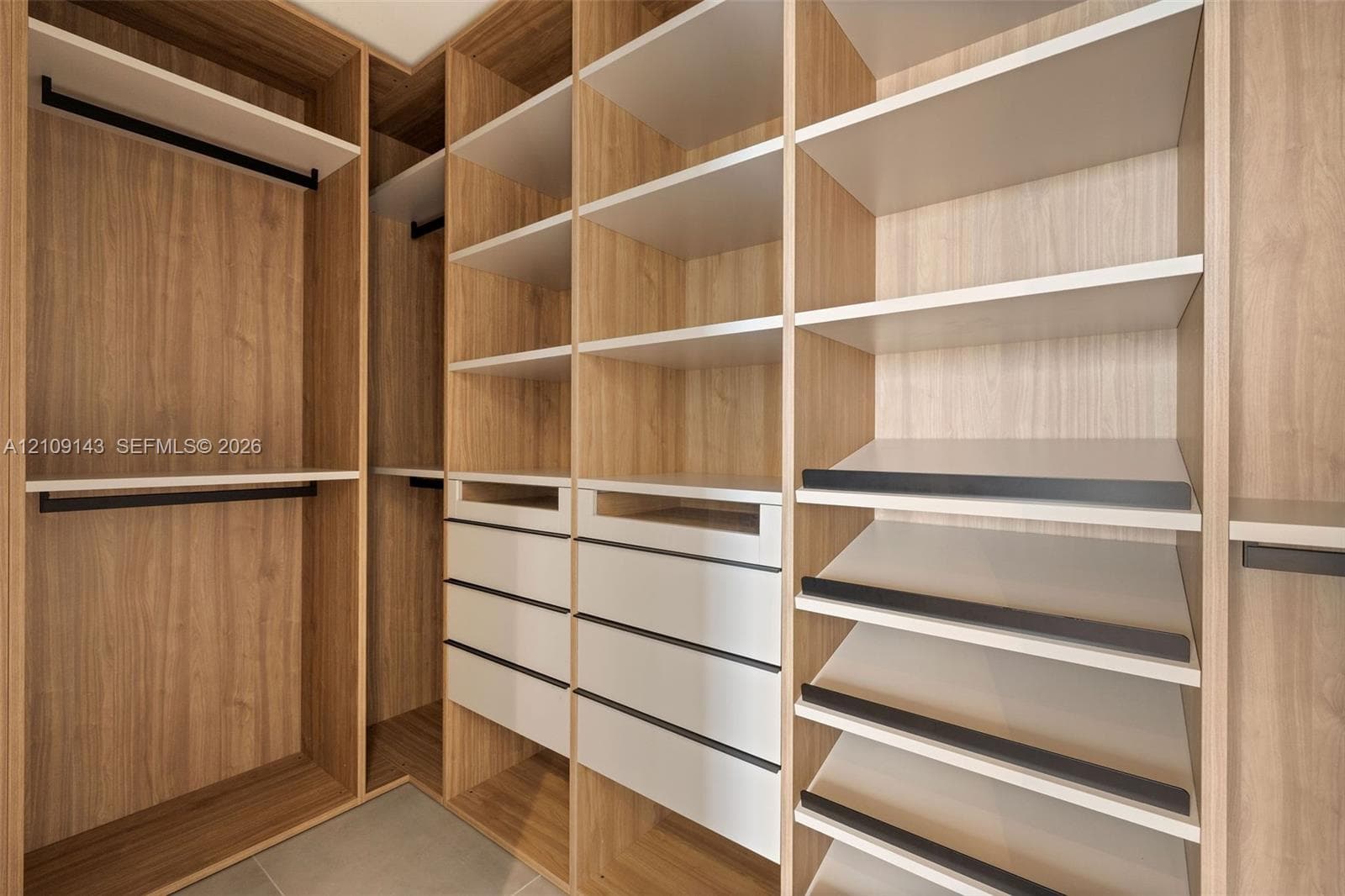 Custom walk-in closet featuring extensive wood-finish shelving, multiple integrated drawers, tiered angled shoe storage, and matte black hanging rods