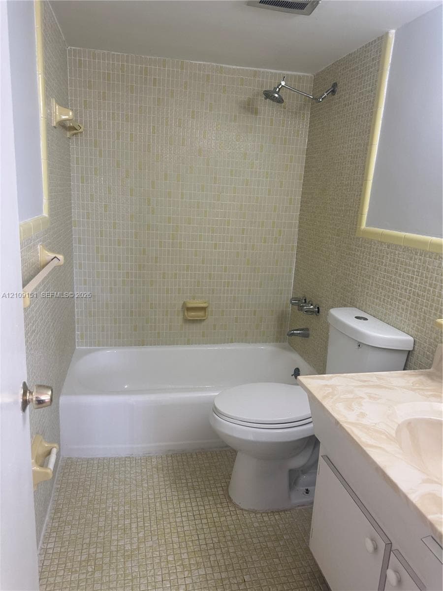 Bathroom featuring full-height mosaic tile surrounds, a white porcelain tub-shower combination, a vanity with a stone-finish countertop, and integrated storage