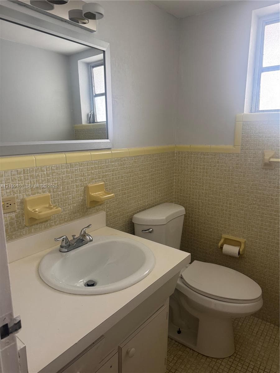 Bathroom featuring a single-sink vanity with a solid surface countertop, ceramic wall tile, built-in recessed soap dishes, and a wall-mounted mirror with integrated lighting