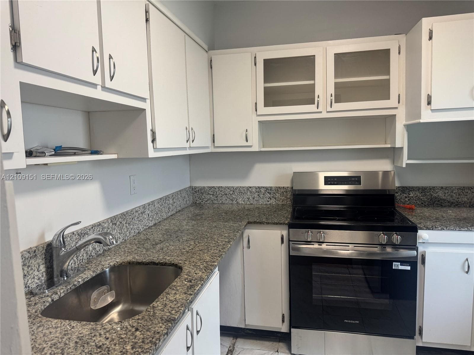 Kitchen featuring white cabinetry with glass-front display uppers, stone countertops, stainless steel undermount sink, and stainless steel freestanding range