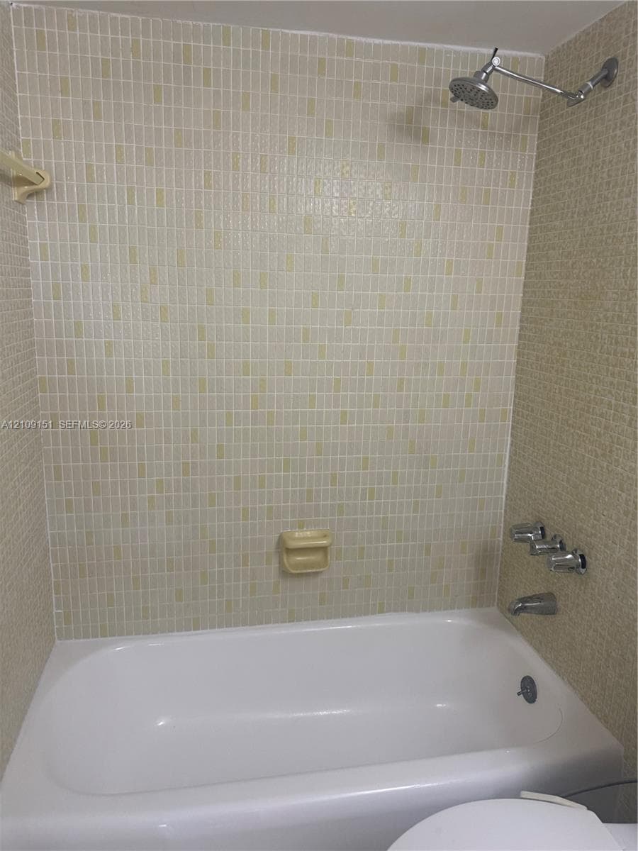 Full-size bathtub featuring integrated wall-mounted shower head, chrome fixtures, and neutral mosaic tile surround