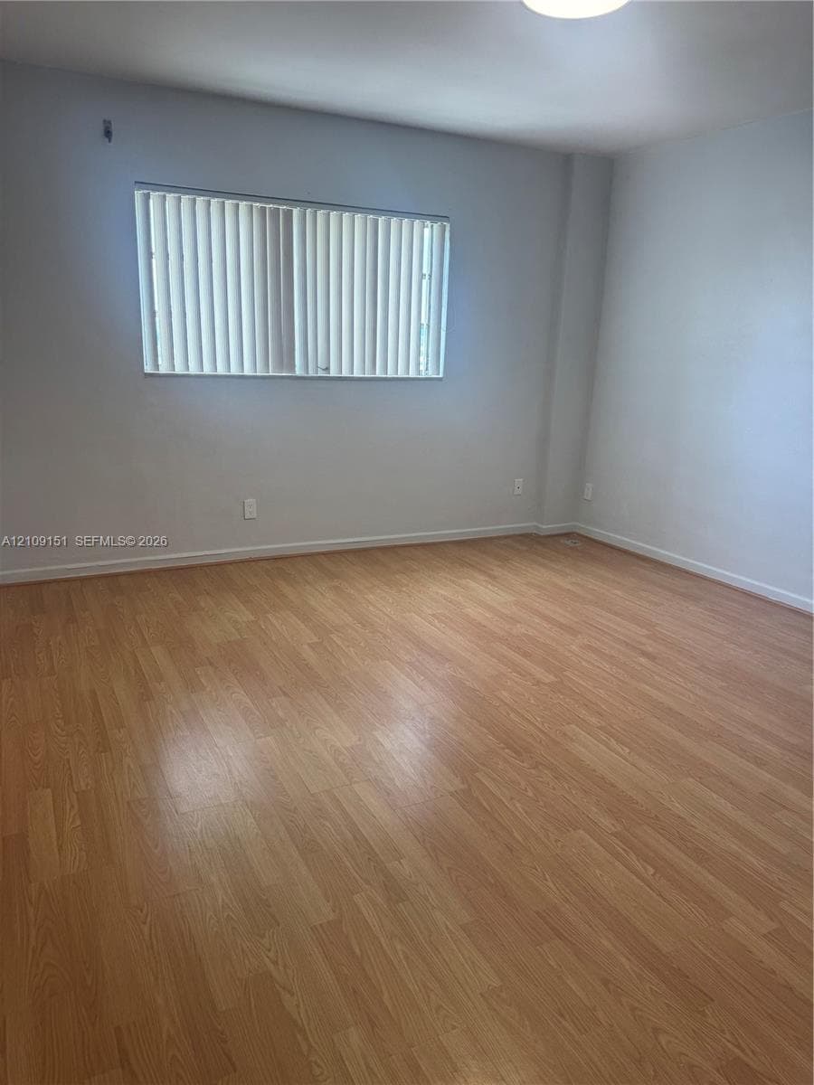 Interior space featuring wood-finish flooring, neutral walls, and a horizontal window with installed vertical blinds