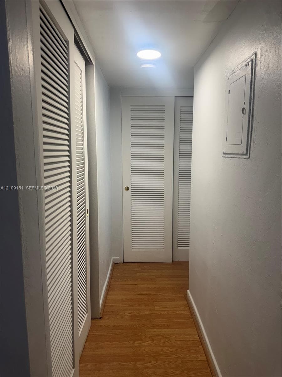 Hallway featuring wood-finish flooring, white walls, and multiple louvered closet doors