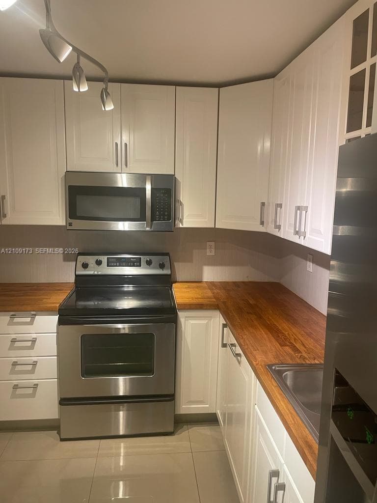Kitchen featuring white cabinetry, wood-finish countertops, stainless steel appliances, and tile flooring