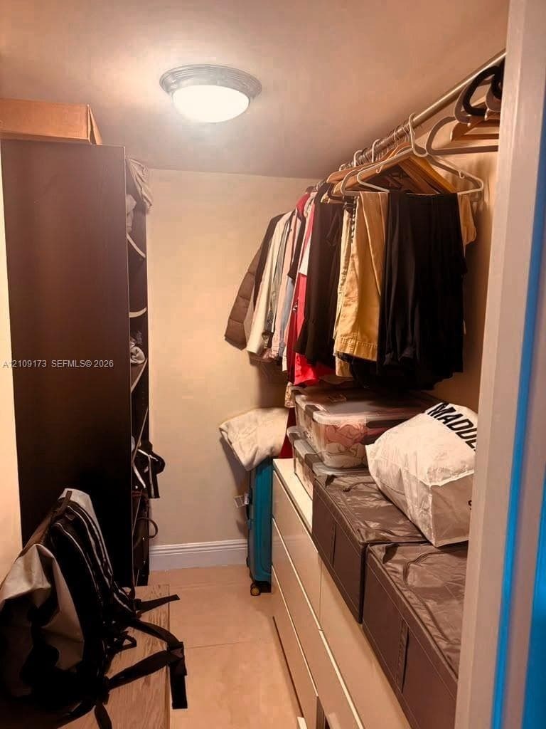 Walk-in storage space featuring built-in shelving, a full-length clothing rod, flush-mount lighting, and tile flooring