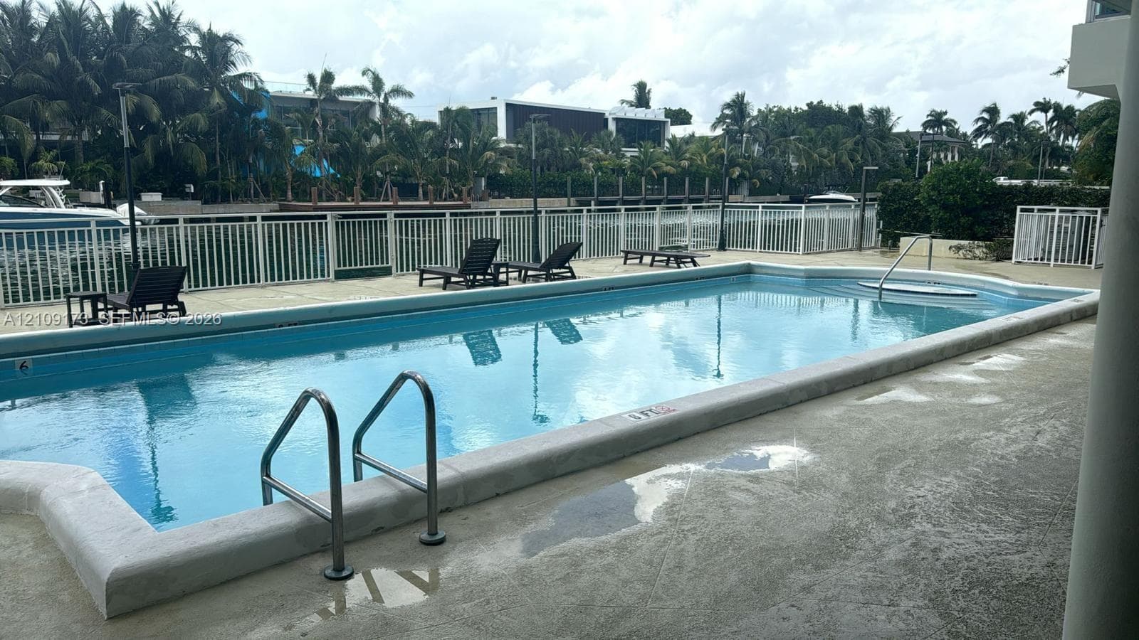 Waterfront pool featuring a concrete deck, built-in metal handrails, and a perimeter safety fence